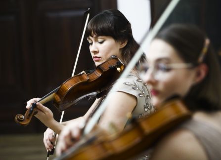 A photograph. A string concert in Villa Decius. Two women play the violin.